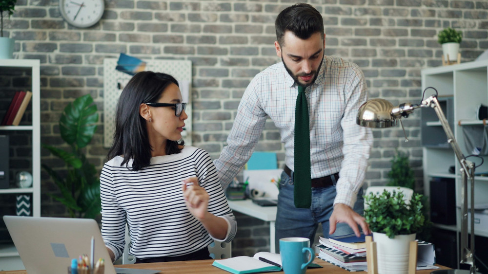 One person interrupts another at her desk