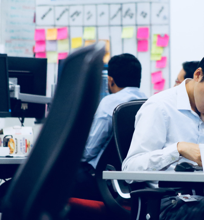 Two man sitting at their computer desks with a Scrum board on the wall behind them