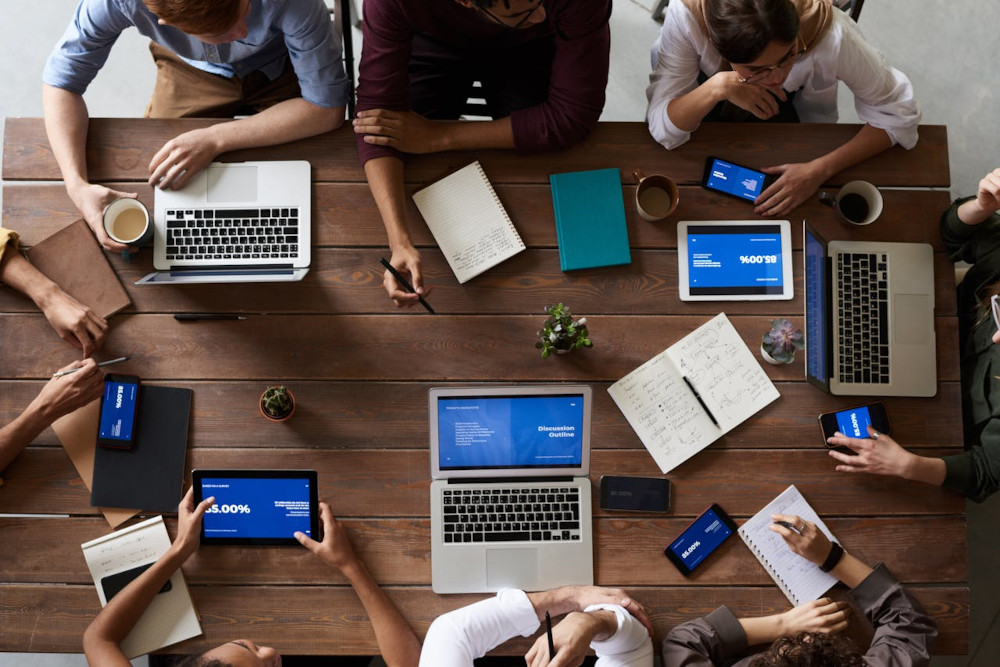 Team in a meeting at a conference table with laptops and smartphones