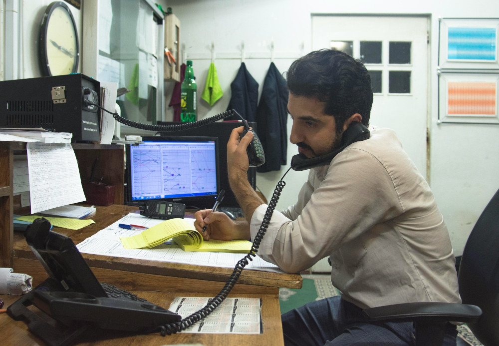 Man at a desk juggling a phone, a notepad and a portable radio communicator