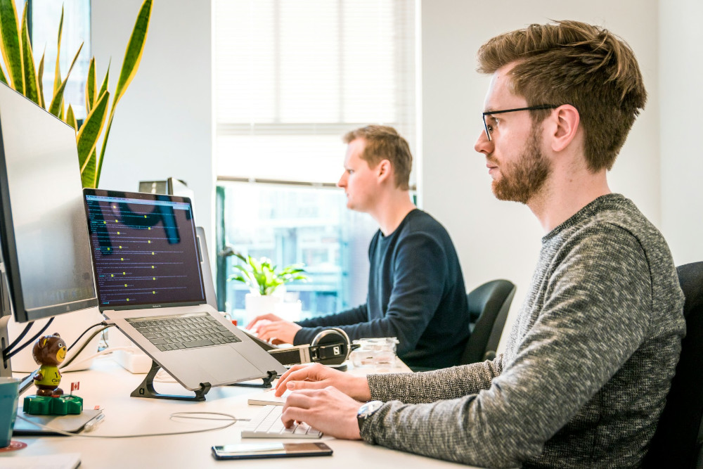 Two men working on laptops at a shared desk