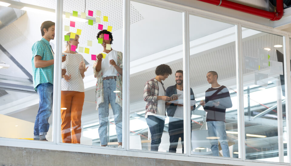 A team discussing tasks written on sticky notes pasted to a window