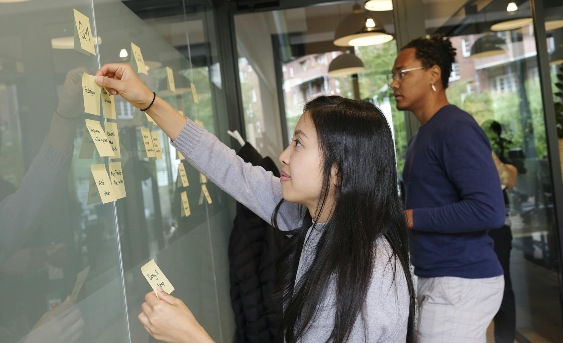 Colleagues plan their tasks represented with sticky notes on an office wall Kanban board