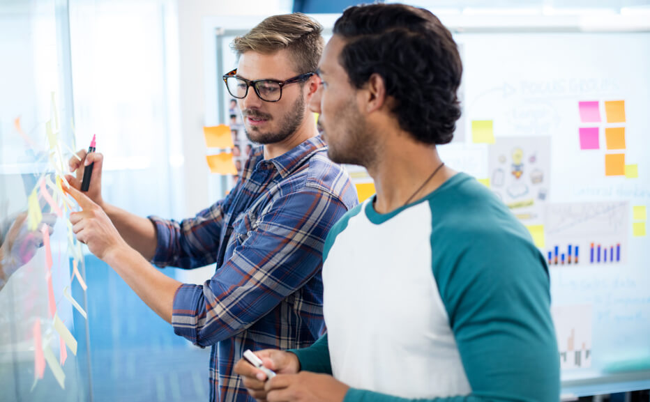 Colleagues planning work on a physical Kanban board with sticky notes for task cards