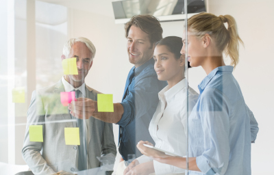 What are Kanban and the Kanban Tool? A team is looking at an office wall with sticky notes making up a Kanban process flow